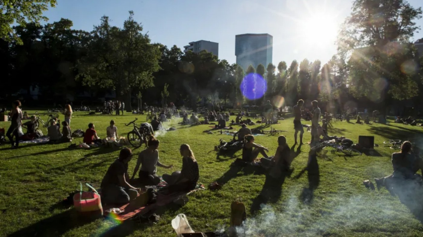 Park in einer Schweizer Stadt, Gegenlicht, Leute auf dem Rasen sitzend