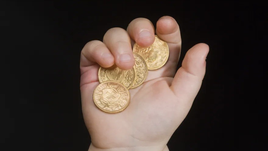 Hand, in der goldene Münzen mit geprägtem Schweizerwappen liegen.