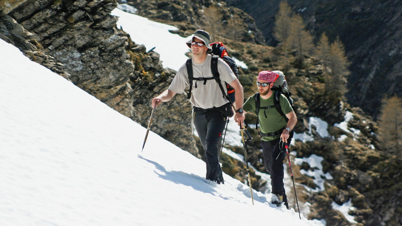 Zwei Wanderer laufen durch Schneefeld, beide mit Wanderstöcken