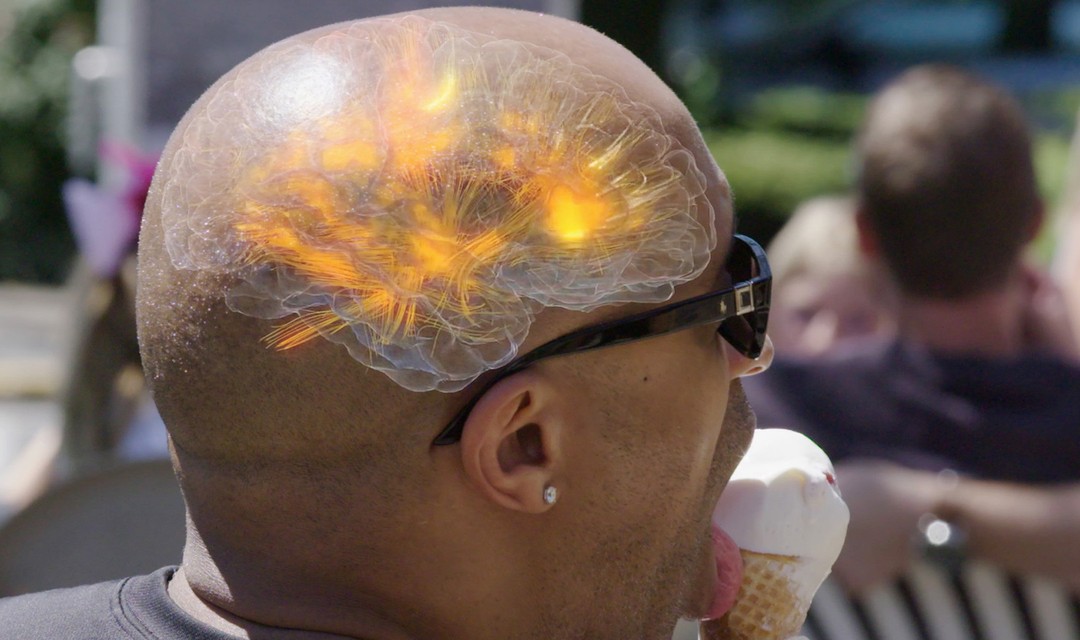 Foto: Ein Mann ist ein Eis. Auf seinem Kopf, an der passenden Stelle, ist halbtransparent eine Computer-Illustration des Gehirns zu sehen.