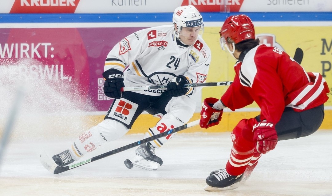Eishockeyspiel, zwei Spieler, einer in weissem Trikot vom HC Lugano, der Gegenspieler in rotem Trikot, der hat den Rücken zur Kamera gedreht