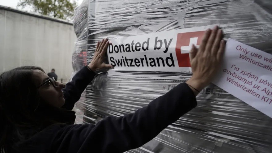 Eine Person klebt einen kleber "Donated by Switzerland" auf ein Paket mit Hilfsleistungen